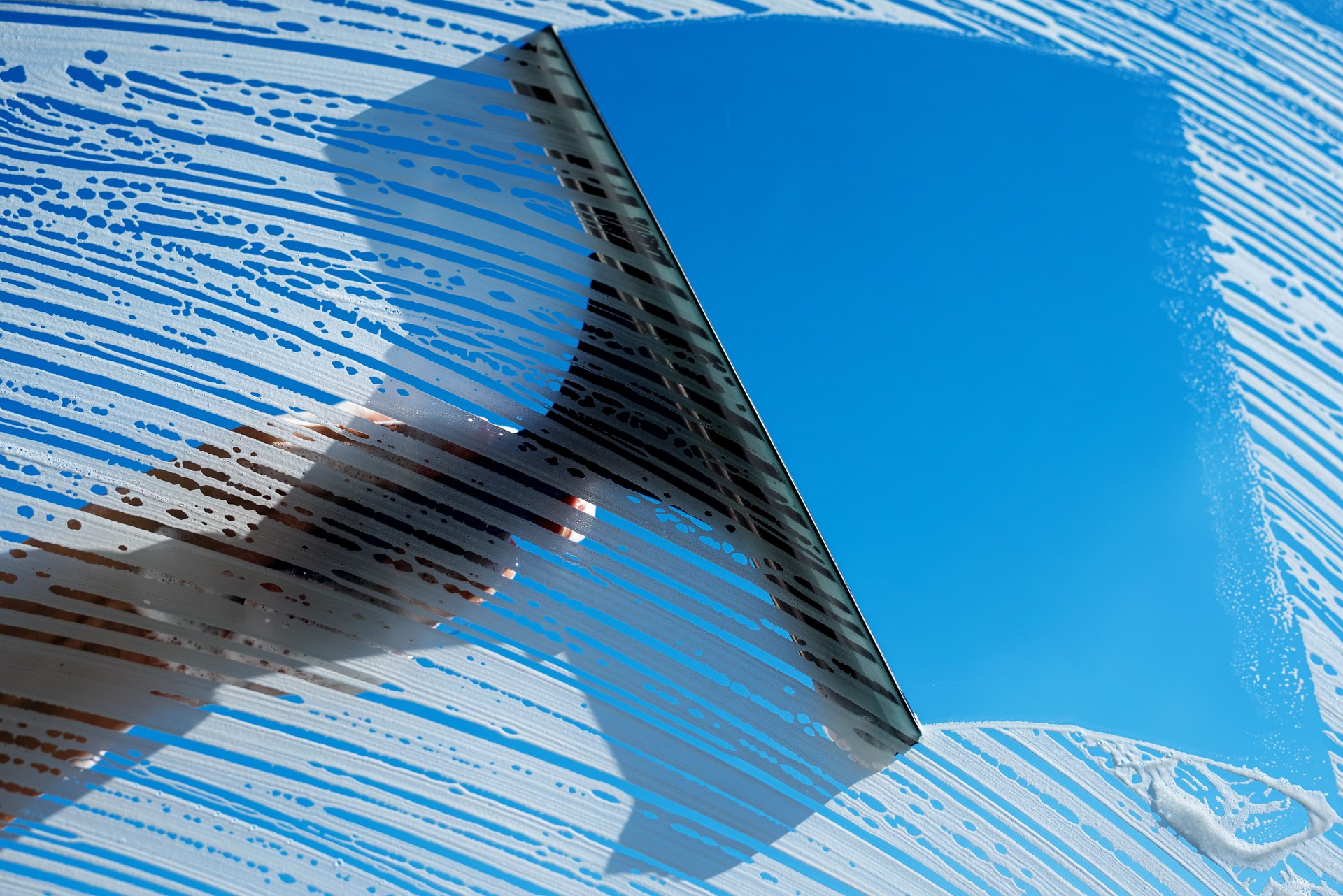 Cleaning soapy windows with squeegee against sunny blue sky. Spring house cleaning concept. Copy space.